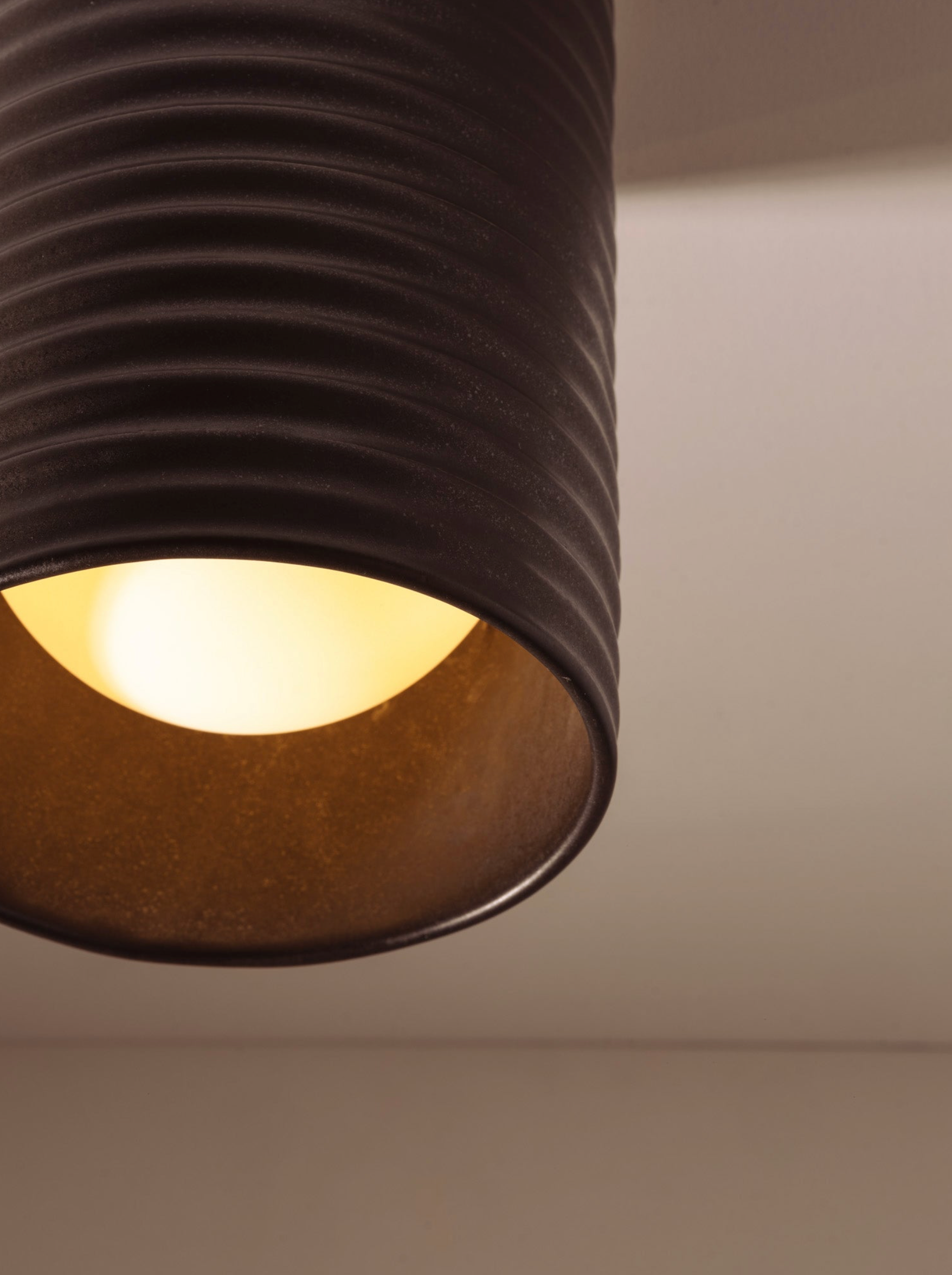 Close-up of a textured brown lampshade with a light bulb inside on a neutral background