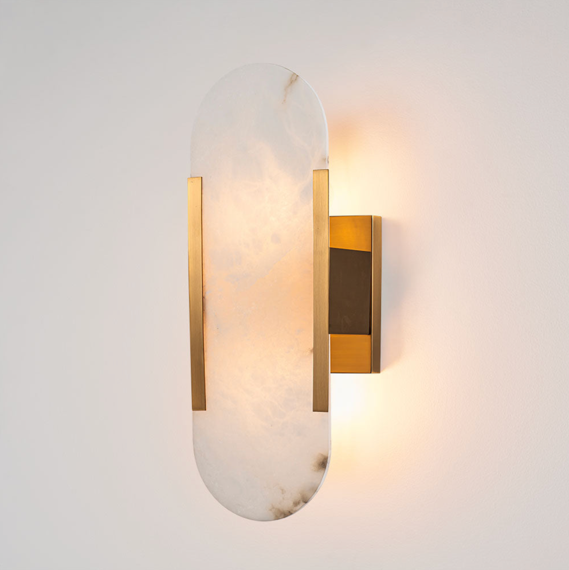 Yves Wall Light brass frame oval alabaster shade illuminated on white wall – Emac & Lawton